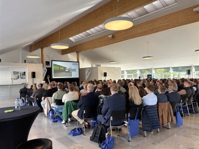 Viele Personen sitzen bei einer Veranstaltung und hören bei einem Vortrag zu.